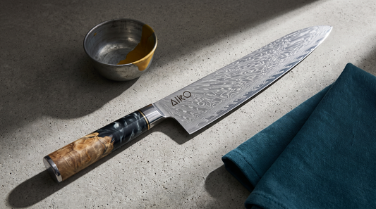 Aiko Black Damascus chef knife on a raw concrete counter, the 67-layer feather pattern catching hard morning light